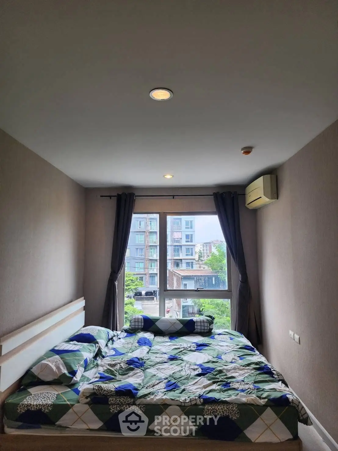 Cozy bedroom with large window and city view, featuring modern decor and air conditioning.