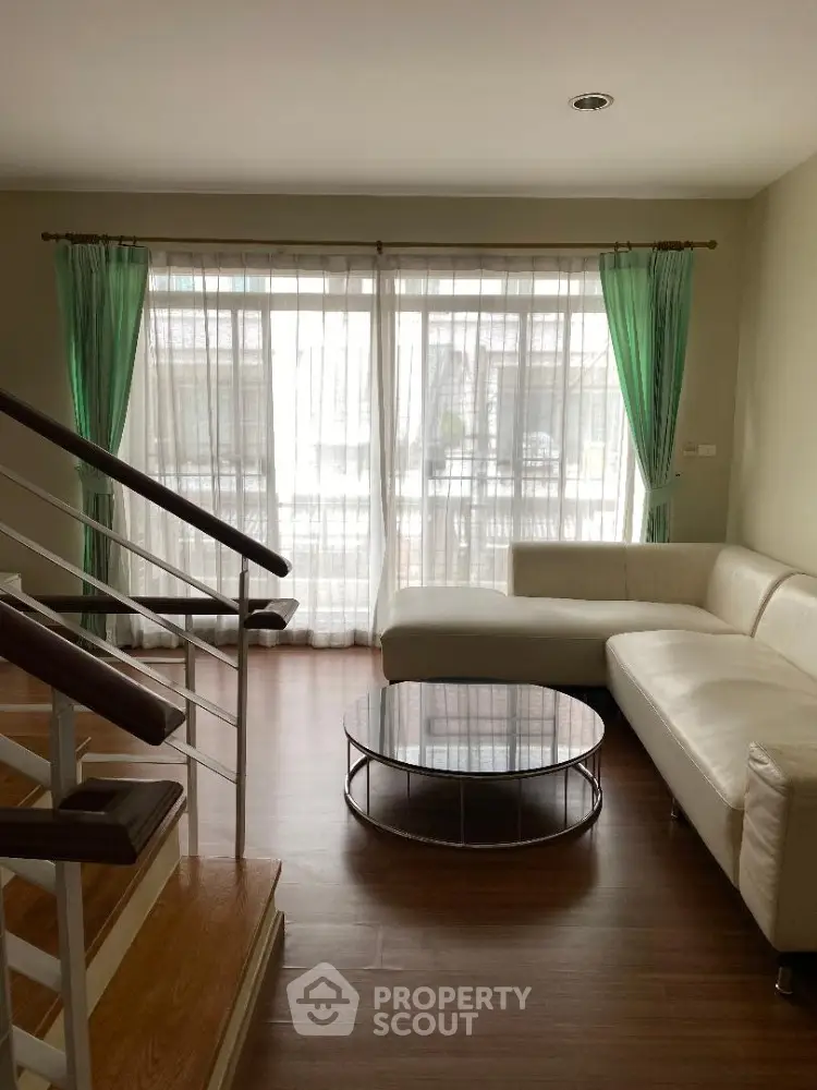 Spacious living room with abundant natural light, elegant hardwood floors, and modern staircase leading to an upper level, perfect for comfortable urban living.