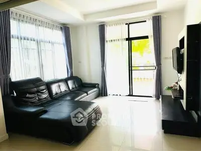 Spacious living room with modern black leather sofa and large windows for natural light.