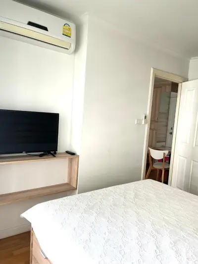 Cozy bedroom with air conditioning and TV, featuring modern wooden furniture and a glimpse into the dining area.