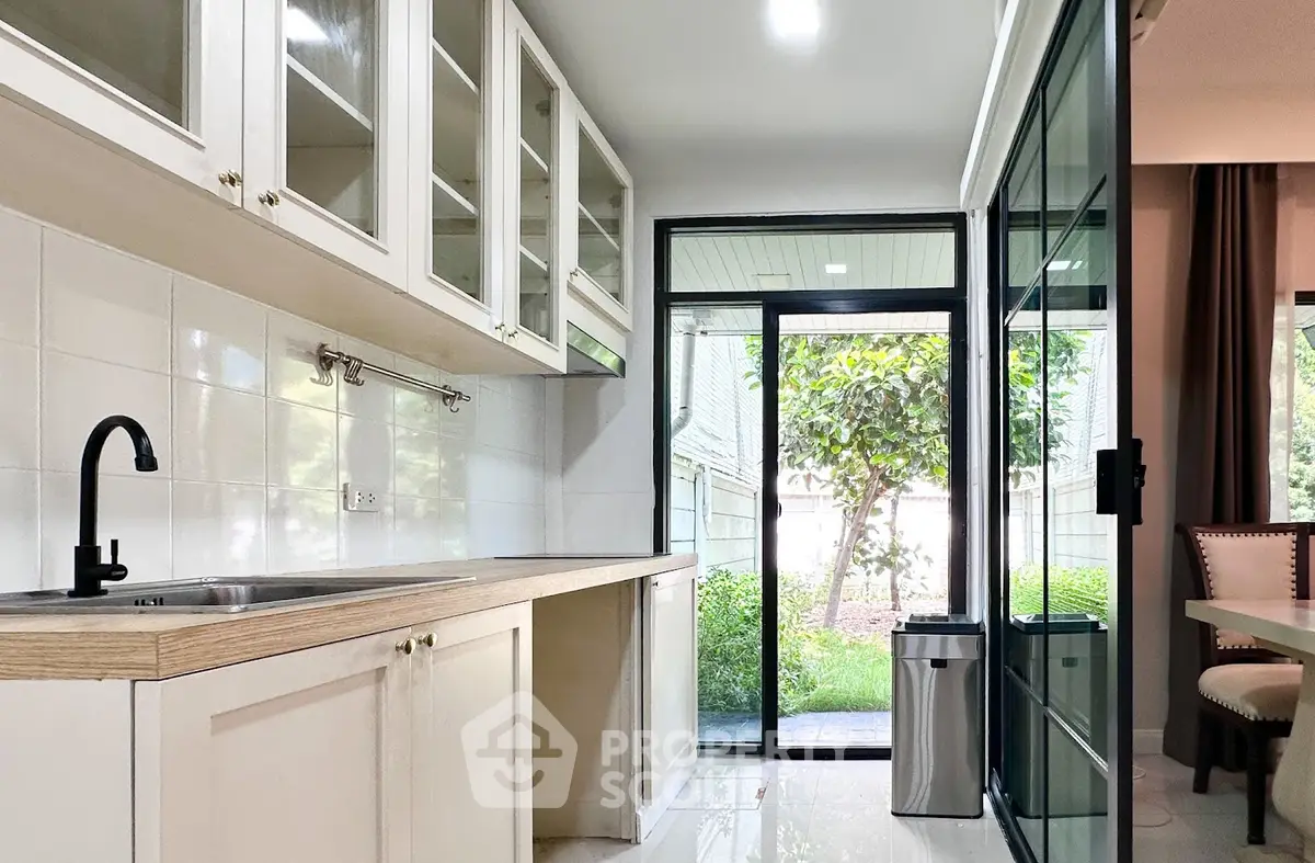 Modern kitchen with open layout and garden view, featuring sleek cabinetry and ample natural light.