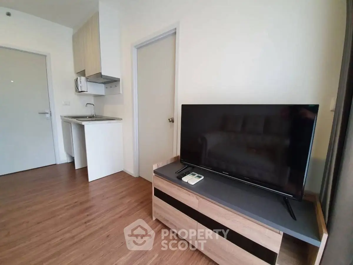 Modern living room with sleek TV stand and compact kitchenette in a cozy apartment.