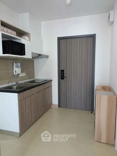Modern compact kitchen with sleek cabinetry and built-in microwave in a contemporary apartment.