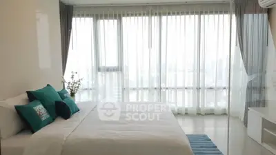 Spacious bedroom with floor-to-ceiling windows and city view, featuring elegant decor and natural light.