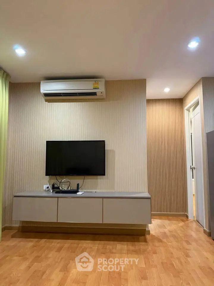 Modern living room with sleek TV setup and wooden flooring, featuring ambient lighting and air conditioning.