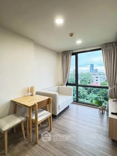 Modern living room with large window offering stunning city view, featuring cozy seating and dining area.