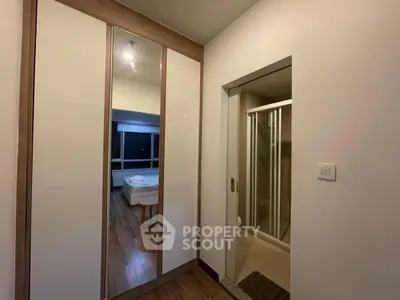 Modern bedroom with mirrored wardrobe and ensuite bathroom, featuring sleek design and wooden flooring.