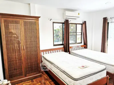 Spacious bedroom with twin beds and wooden wardrobe, featuring natural light and air conditioning.