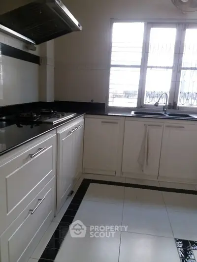 Modern kitchen with white cabinetry and gas stove, ample natural light from large window.