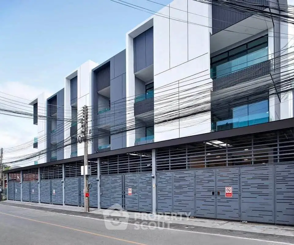 Modern multi-story building with sleek design and secure gated entrance on a quiet street.