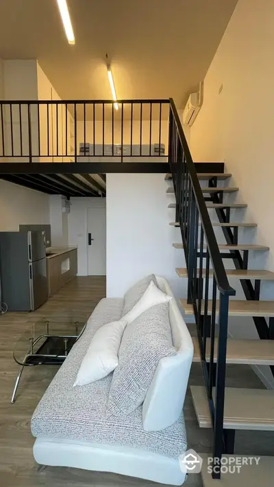 Modern loft apartment with high ceilings, sleek metal staircase leading to an upper level, and a cozy living area with stylish furnishings and integrated kitchen appliances.