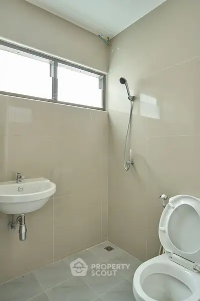 Modern bathroom with sleek fixtures and neutral tiles, featuring a wall-mounted sink and shower.