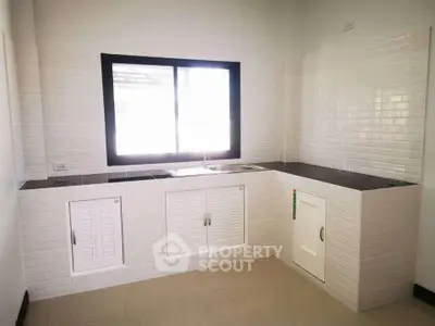 Modern kitchen with sleek white cabinetry and large window for natural light.