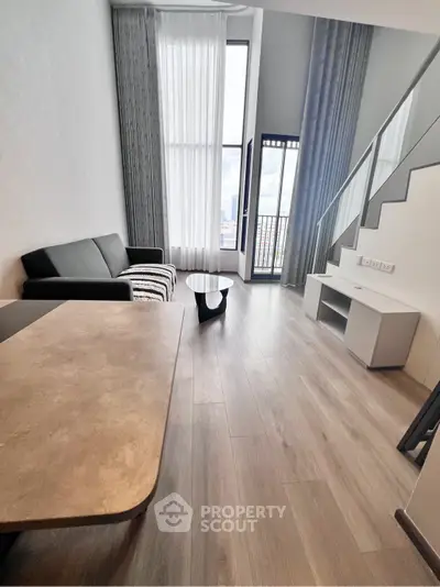 Modern living room with high ceilings and large windows offering city views.