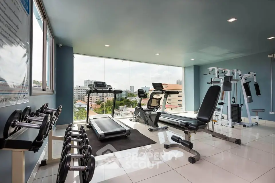 Modern gym with city view, equipped with treadmills, exercise bikes, and weights, perfect for fitness enthusiasts.
