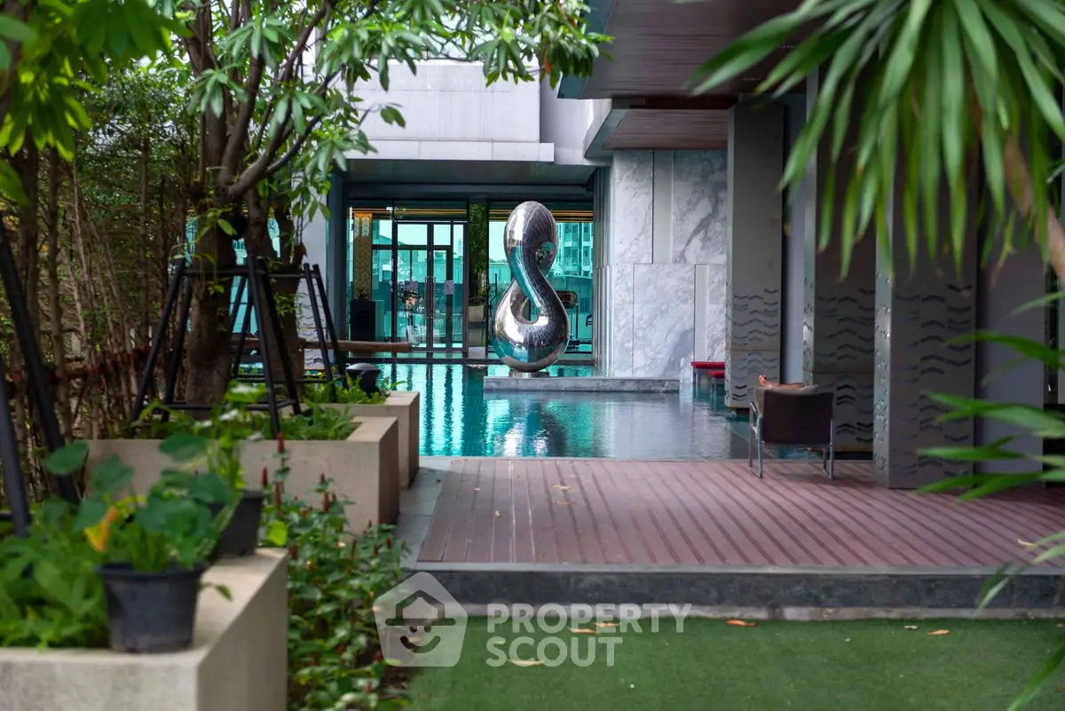Luxurious pool area with modern sculpture and lush greenery in upscale residential complex.
