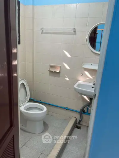 Compact bathroom with basic fixtures and blue accents, featuring a toilet, sink, and small mirror.