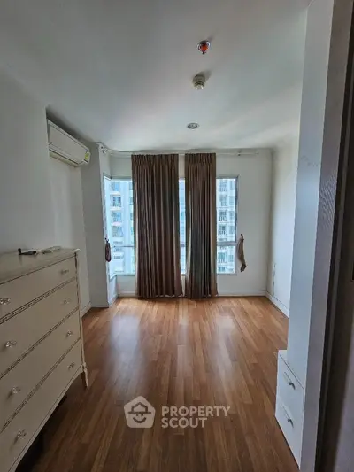 Spacious bedroom with wooden flooring and large windows offering city views.