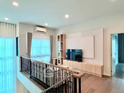 Modern living room with stylish decor and natural light, featuring a sleek TV setup and elegant railing.