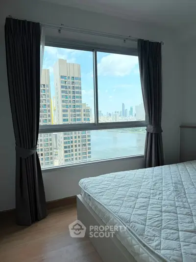 Modern bedroom with stunning city and river view from large window, featuring elegant curtains and wooden flooring.