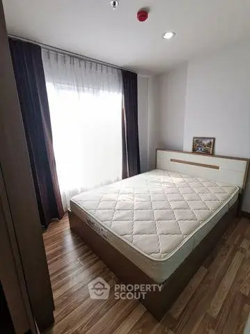 Cozy bedroom with natural light and wooden flooring, featuring a comfortable bed and elegant curtains.