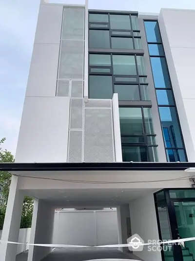 Sleek modern architecture defines this stunning urban residence, boasting expansive glass windows, a striking white facade, and a spacious covered parking area.