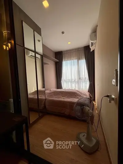 Cozy bedroom with wooden flooring, mirrored wardrobe, and natural light from large window.