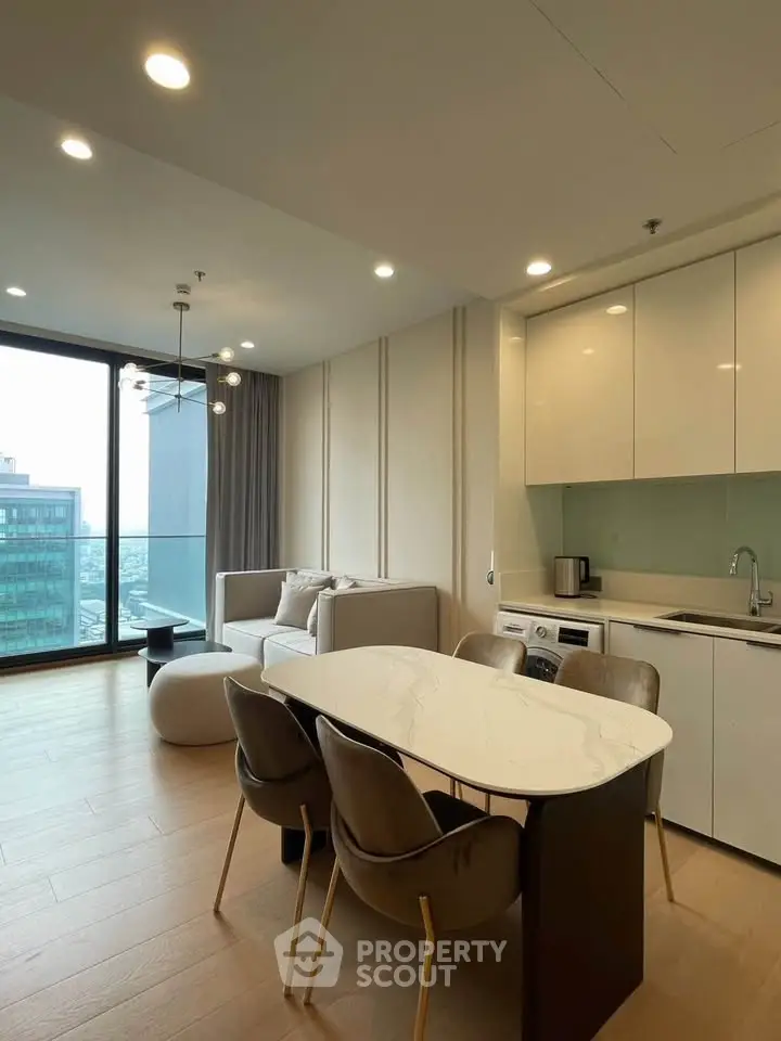 Modern open-plan living room with kitchen and city view, featuring sleek furniture and large windows.