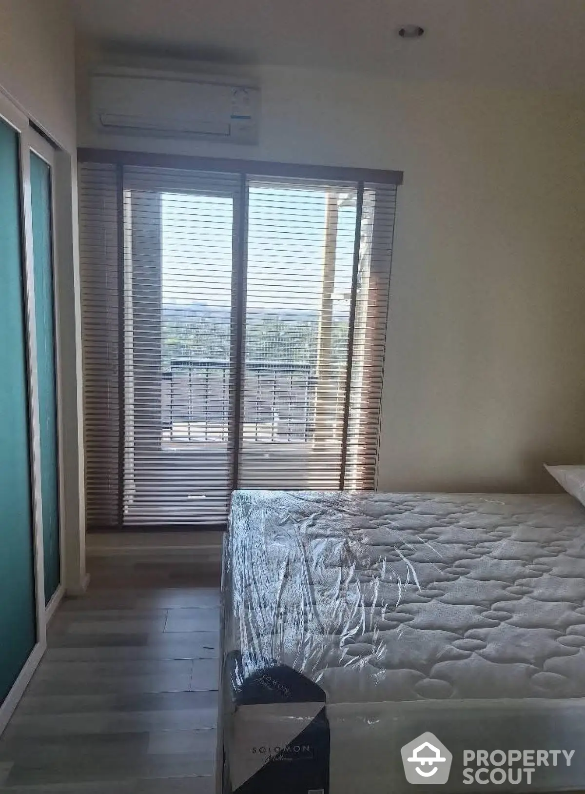 Bright bedroom with balcony access and air conditioning, featuring a new mattress and modern blinds.