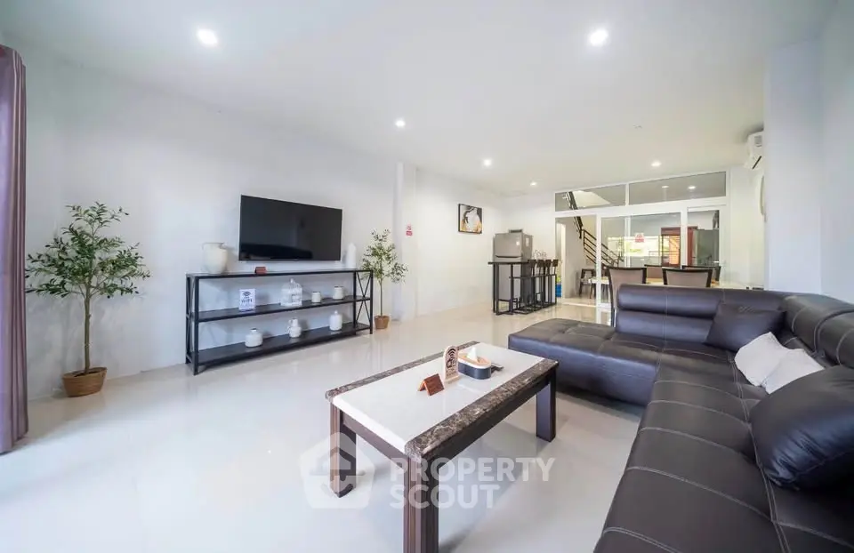 Spacious modern living room with sleek leather sofa and large TV, perfect for relaxation.
