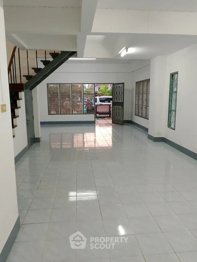 Spacious open-plan living area with tiled floors and staircase, ample natural light.