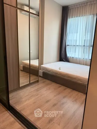 Modern bedroom with mirrored closet and large window, featuring elegant curtains and wooden flooring.