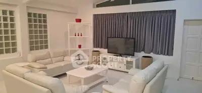 Spacious modern living room with white leather sofas and large TV, perfect for relaxation and entertainment.
