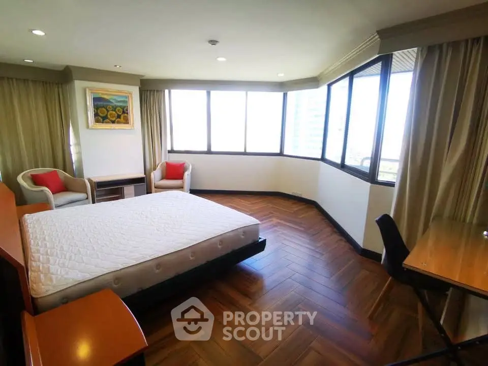 Spacious bedroom with large windows and elegant wood flooring in a modern apartment.