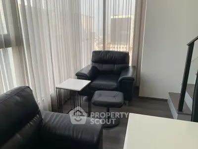 Modern living room with sleek black leather furniture and large windows offering natural light.