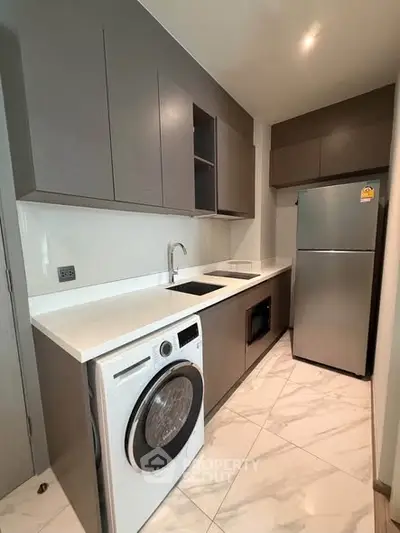 Modern kitchen with sleek cabinetry, washing machine, and stainless steel fridge in a compact layout.