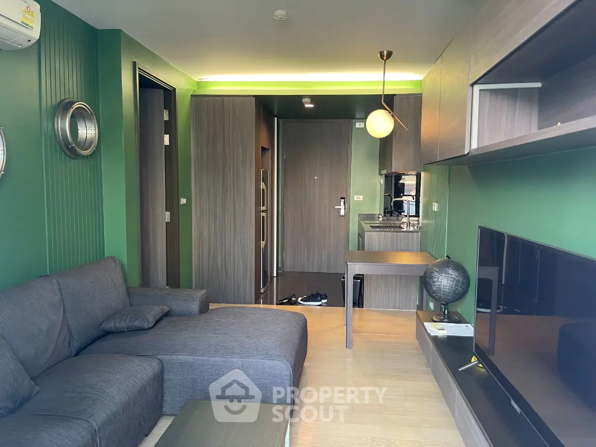 Modern living room with green walls, stylish furniture, and open kitchen layout in a contemporary apartment.