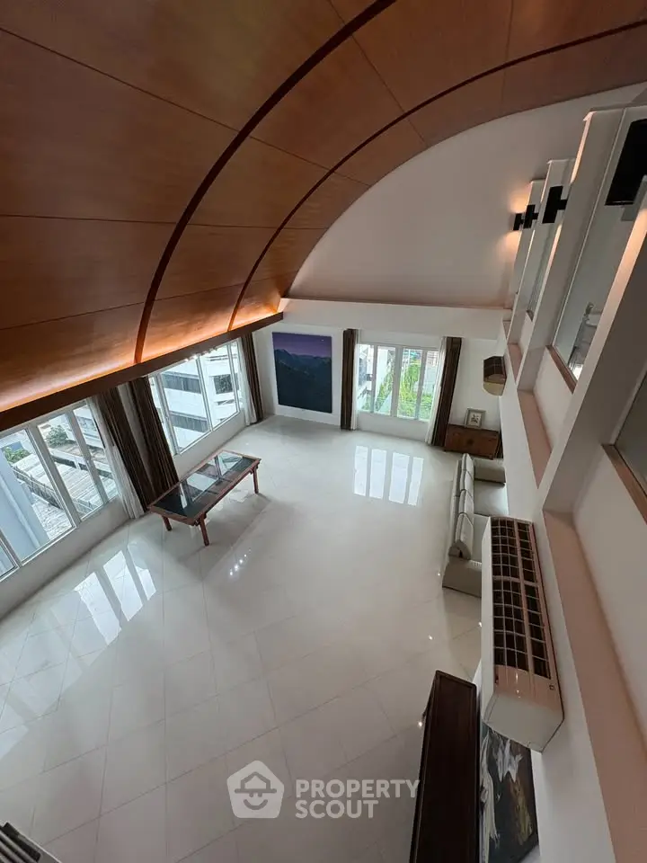 Spacious modern living room with high ceiling and large windows offering city views.