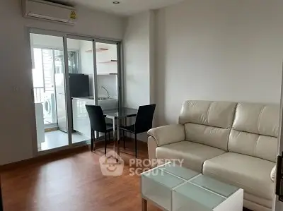 Modern living room with white sofa and glass table, adjacent to a compact kitchen with washing machine.