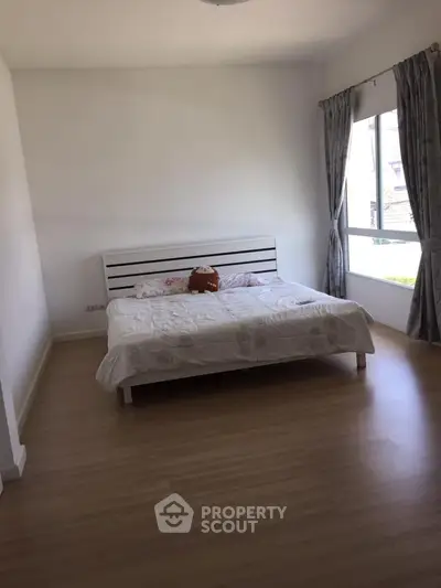 Spacious bedroom with large window and wooden flooring in modern home