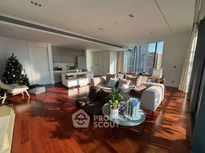 Spacious modern living room with open kitchen and city view, featuring elegant decor and natural light.