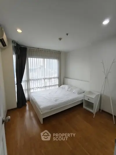 Spacious bedroom with large window and wooden flooring in modern apartment.