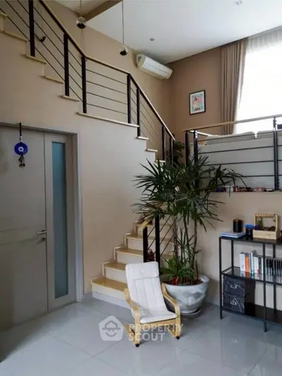Modern living room with stylish staircase and indoor plant, featuring sleek design and natural light.
