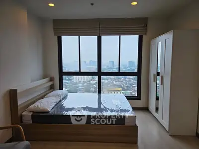 Modern bedroom with large window offering city view, featuring a bed and wardrobe.