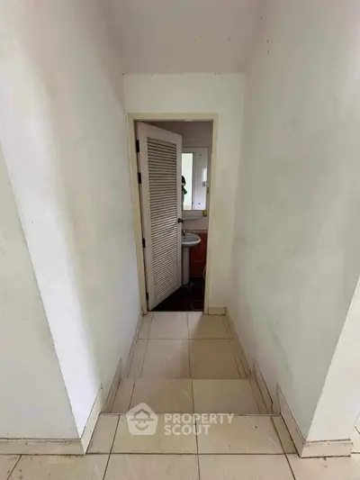 Narrow hallway leading to a small bathroom with a louvered door and tiled floor.