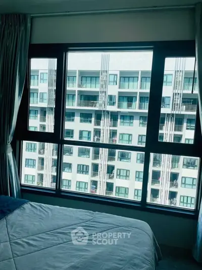 Spacious bedroom with large window offering a stunning view of modern apartment complex.