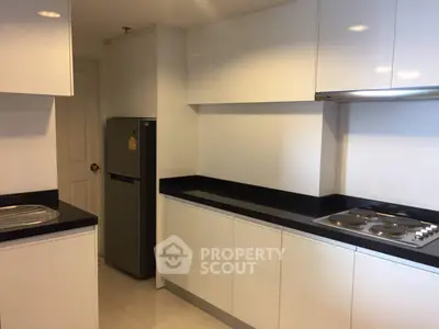 Modern kitchen with sleek white cabinets and black countertops, featuring an electric stove and stainless steel fridge.