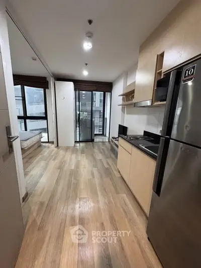 Modern apartment interior with open kitchen and wooden flooring, featuring a sleek fridge and balcony view.