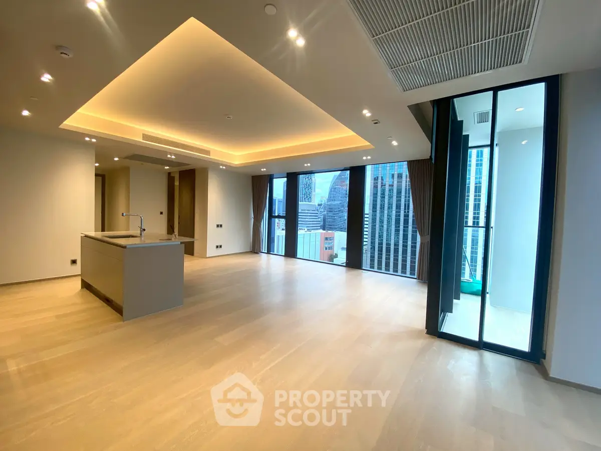 Spacious modern living room with open kitchen and city view, featuring elegant lighting and large windows.