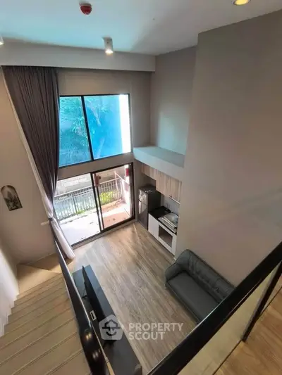 Modern loft-style living room with high ceilings and large windows, featuring a cozy sofa and sleek wooden flooring.